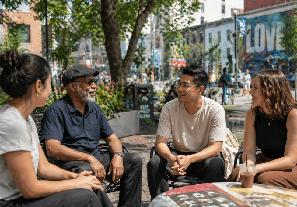 Multi-generational group talking together in a neighborhood public space, illustrating civic capacity, strong social ties, and community relationships that support long-term health outcomes